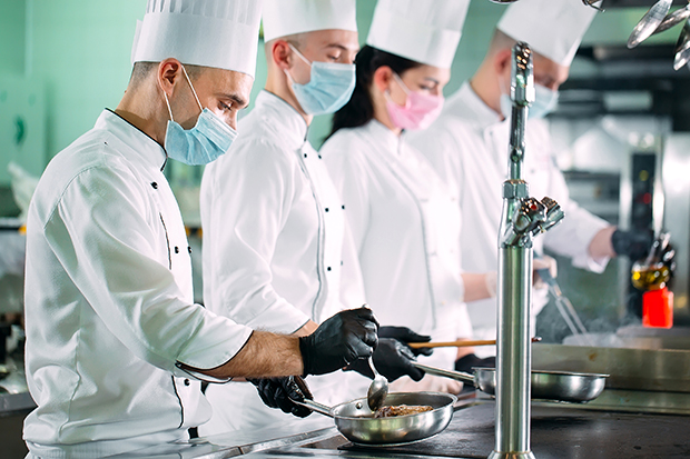 Chefs in protective masks and gloves prepare food in the kitchen
