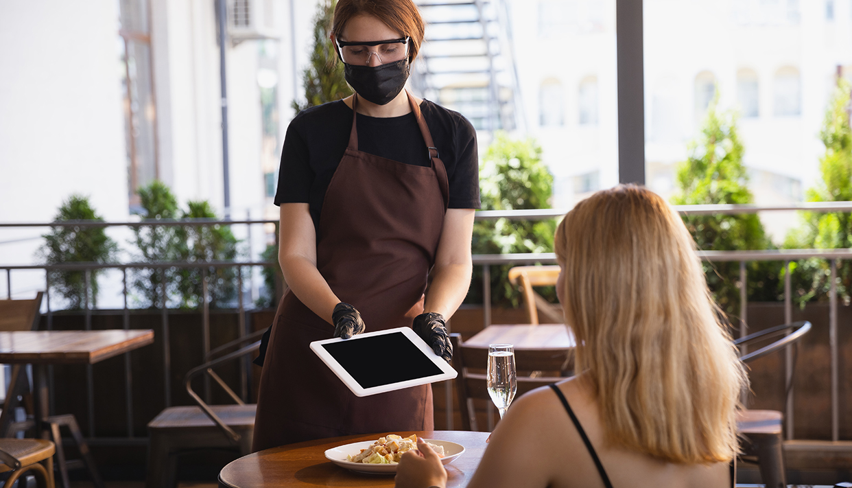 The waitress works in a restaurant in a medical mask, gloves during coronavirus pandemic