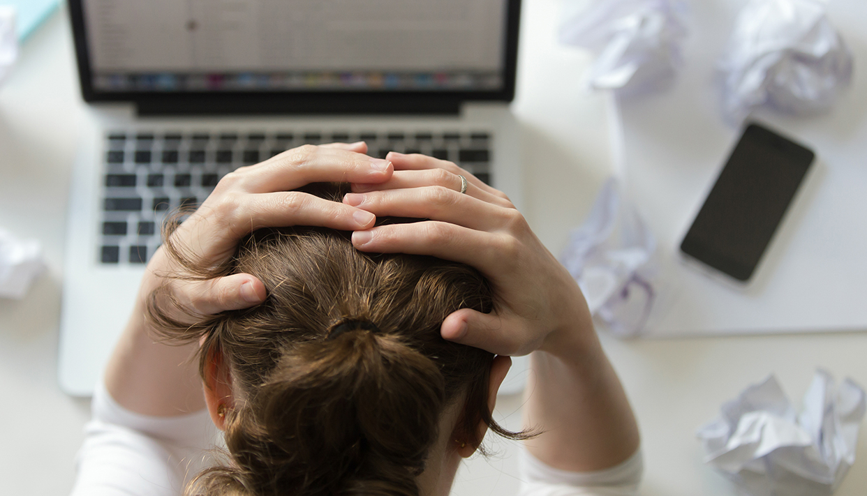 Portrait of a woman grabbing head at desk near the laptop