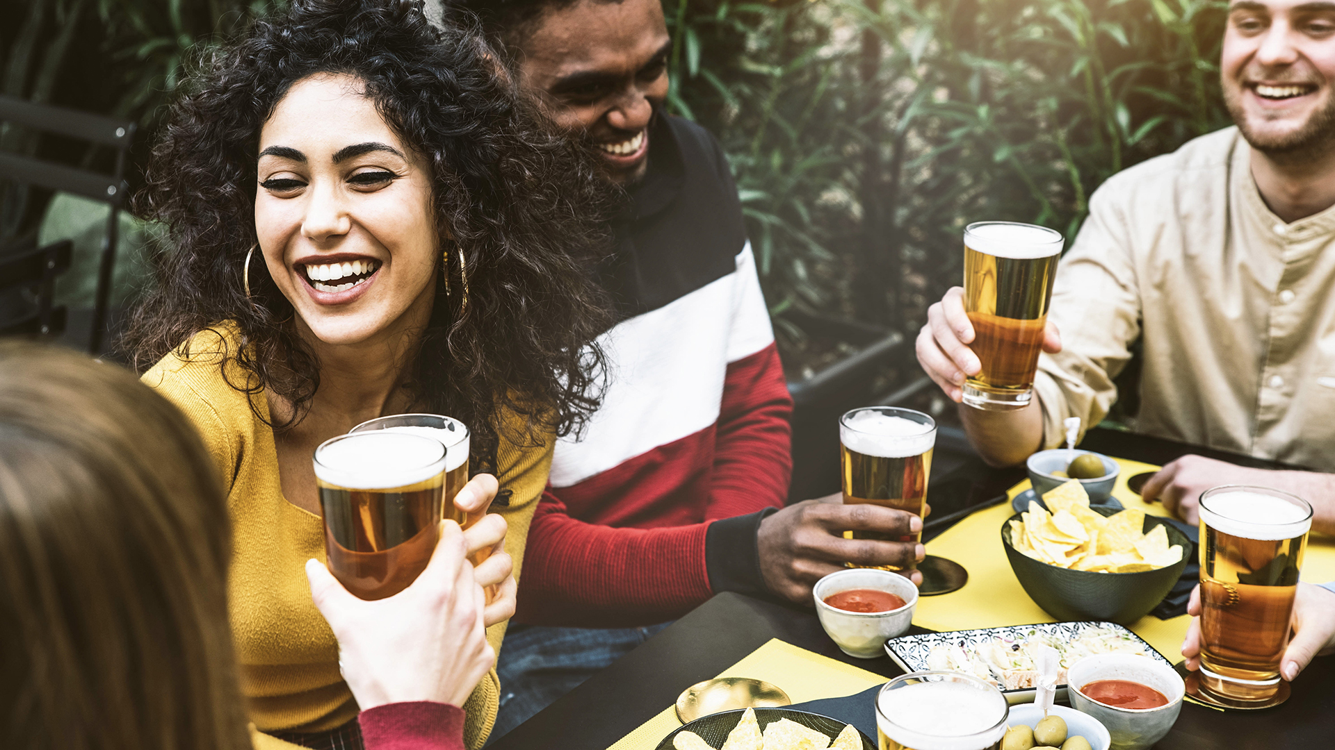 Multi-ethnic friends enjoying happy hour drinking beer at brewery pub – Group of young people celebrating weekend having an aperitif at bar restaurant – Beverage lifestyle and friendship concept
